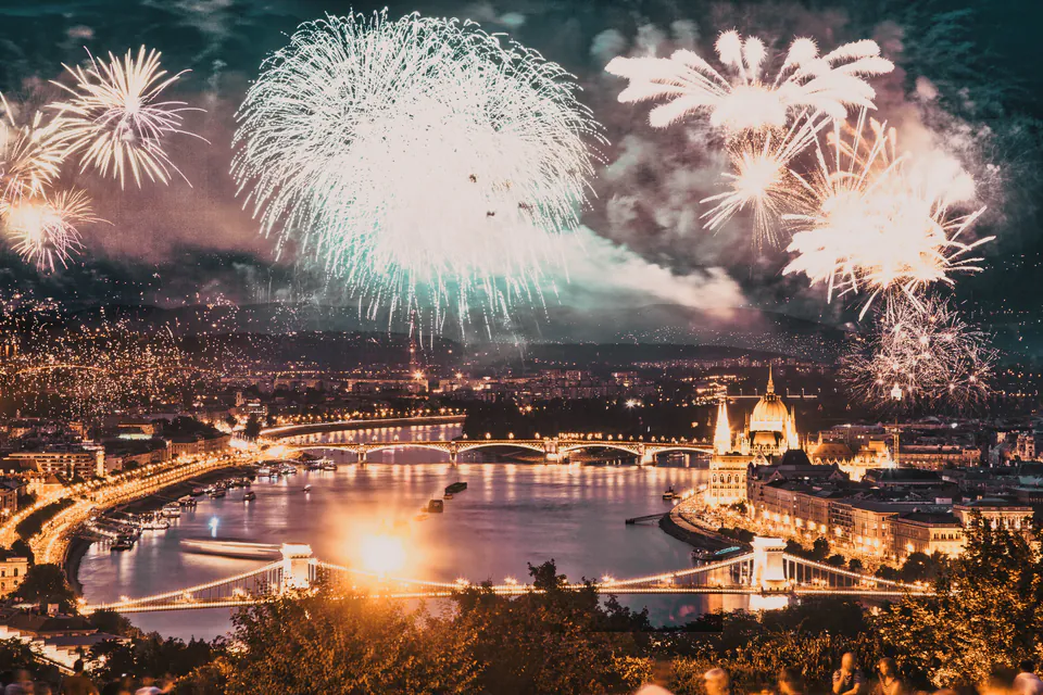 Fireworks illuminate Budapest's skyline over the Danube River, with Parliament and Chain Bridge visible below