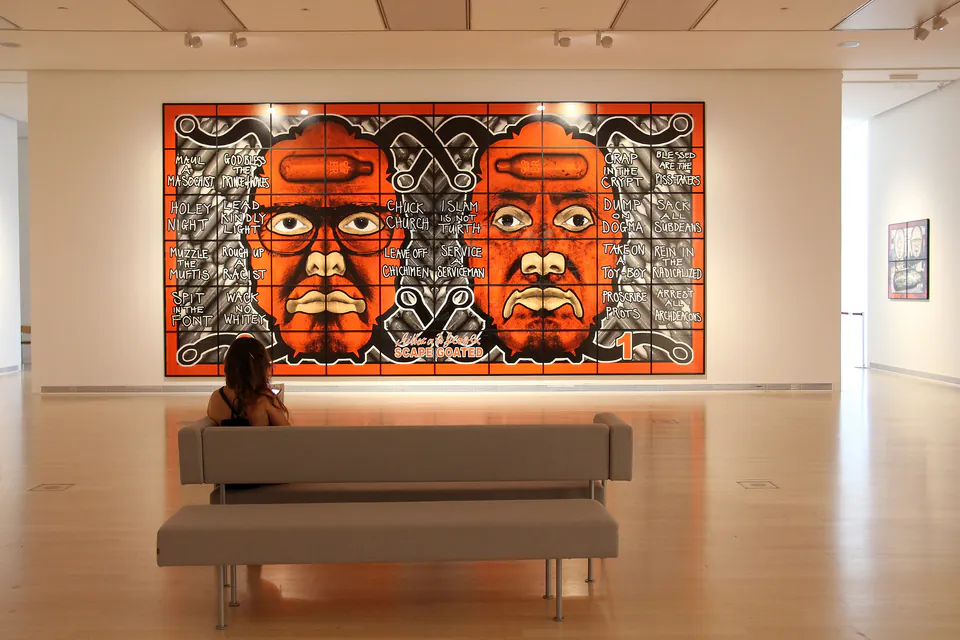 Large orange and black mural artwork with text elements displayed in bright gallery space