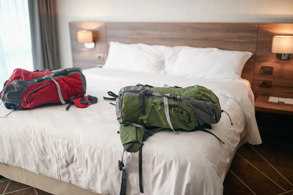 Modern hotel-style room with backpacks on clean white bed