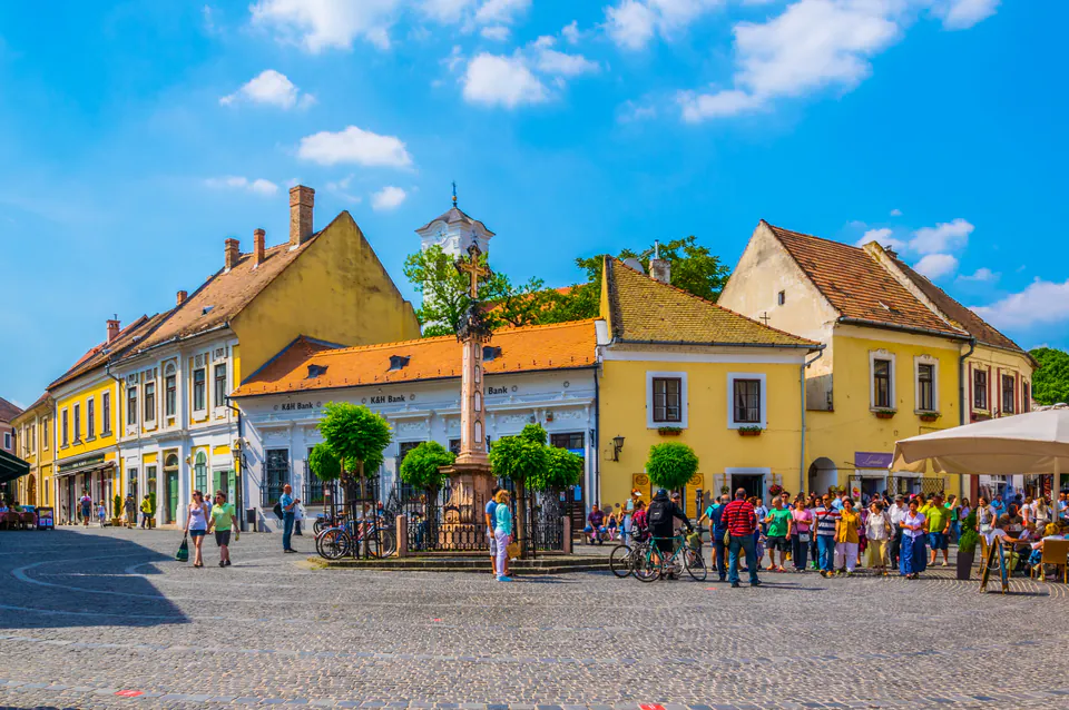 Historic main square in Szentendre with yellow baroque buildings and central monument under blue sky