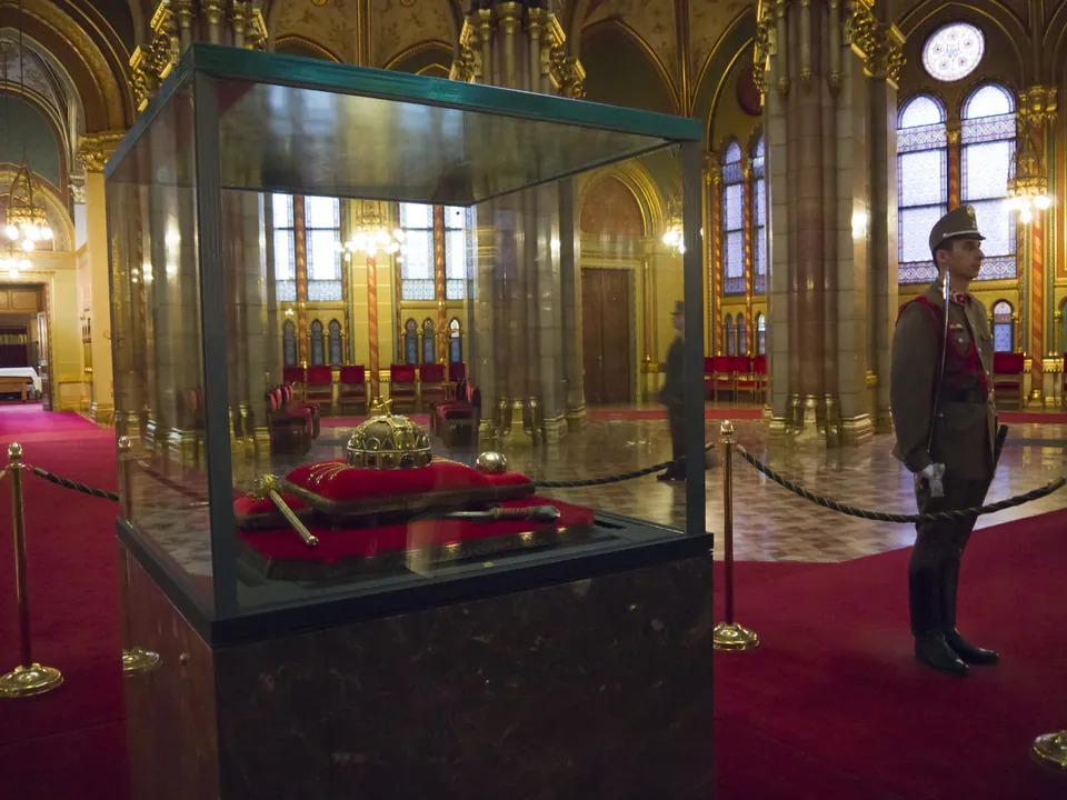 Ornate hall with glass display case containing crown jewels and ceremonial guard standing watch