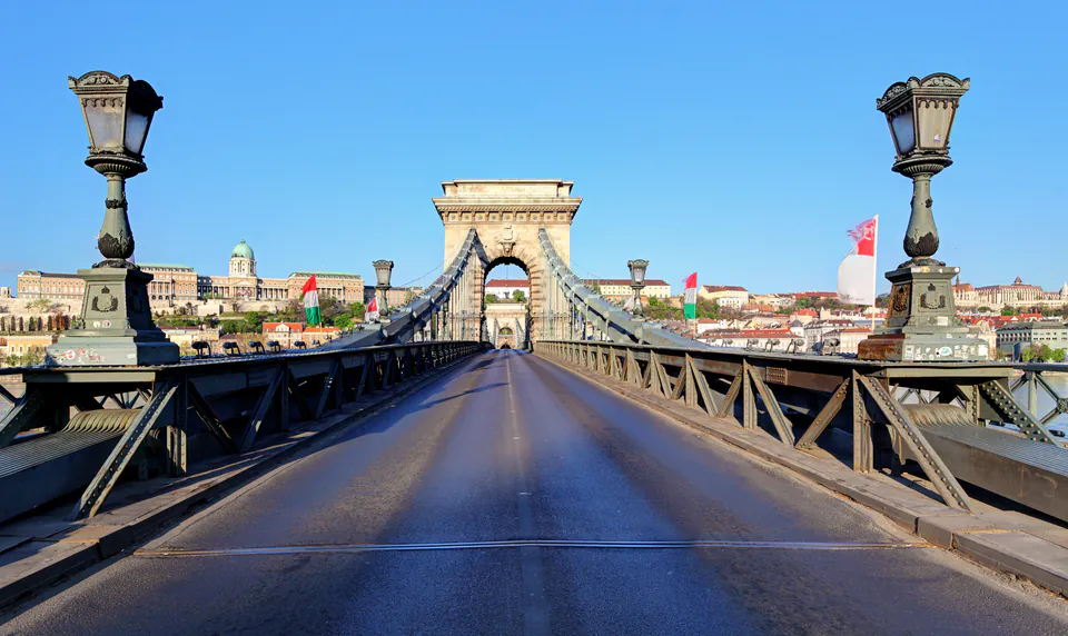 Empty roadway on Chain Bridge with ornate lampposts and Buda Castle in background