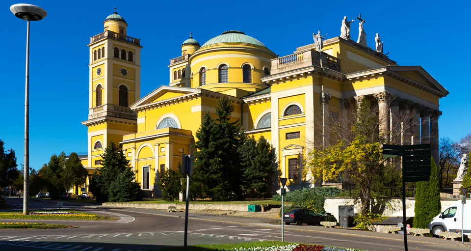 Yellow neoclassical Eger Basilica with twin towers and central dome against blue sky