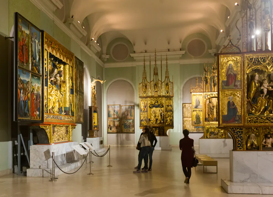 Visitors viewing medieval religious artwork and altarpieces in museum gallery
