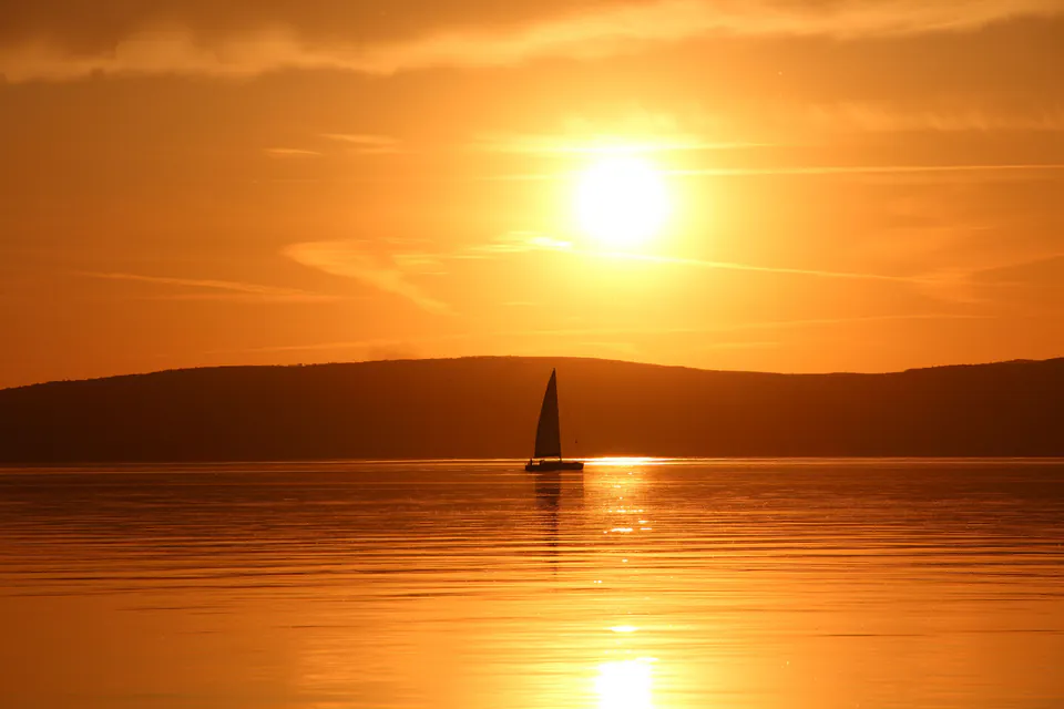 Sailboat silhouetted against golden sunset over Lake Balaton with hills in background
