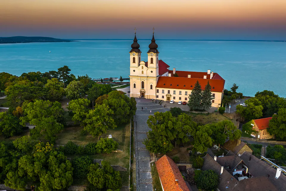 Historic Tihany Abbey overlooking Lake Balaton at sunset with twin towers and red roofs