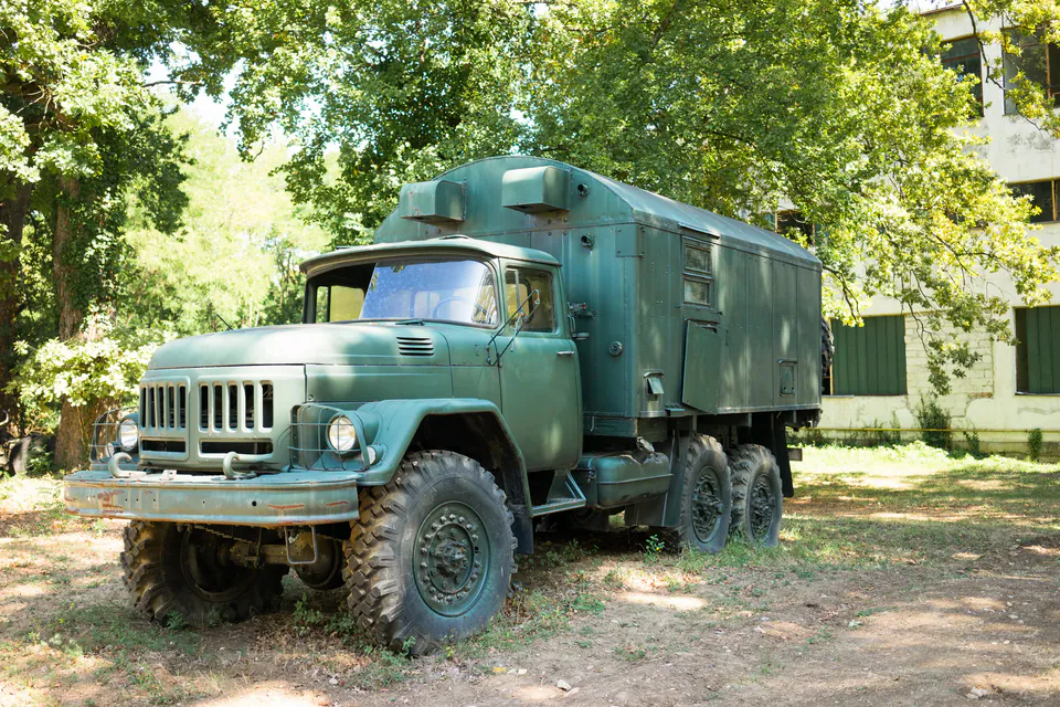 Vintage green Russian military truck from the Cold War era parked under trees