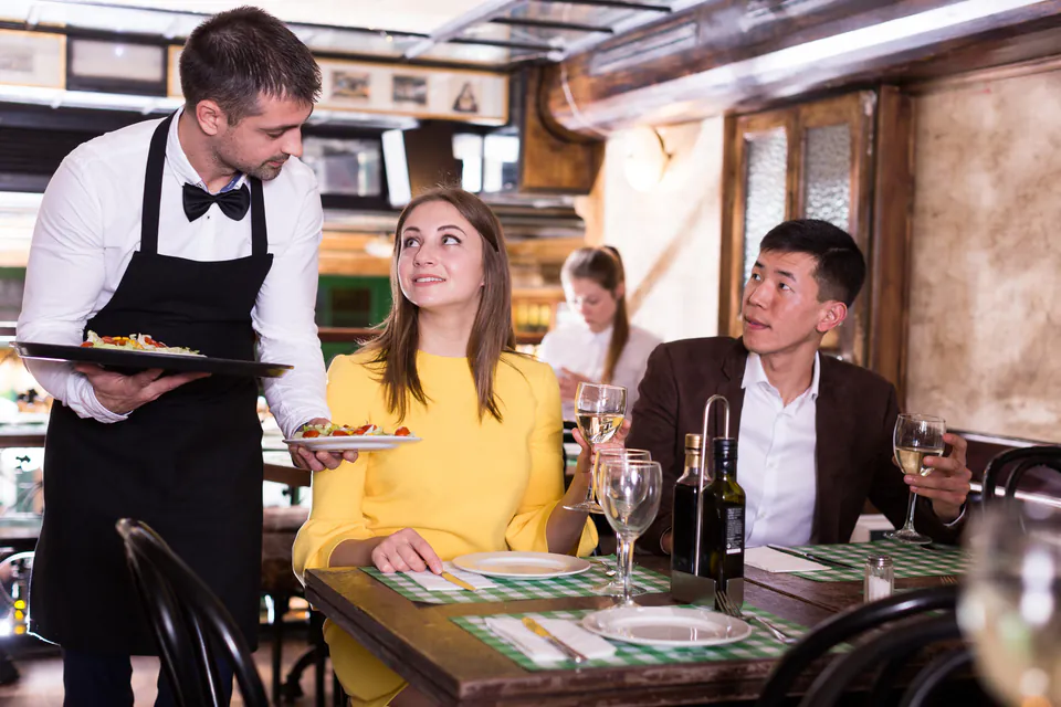 Restaurant server in formal attire serving plates to diners in an upscale setting