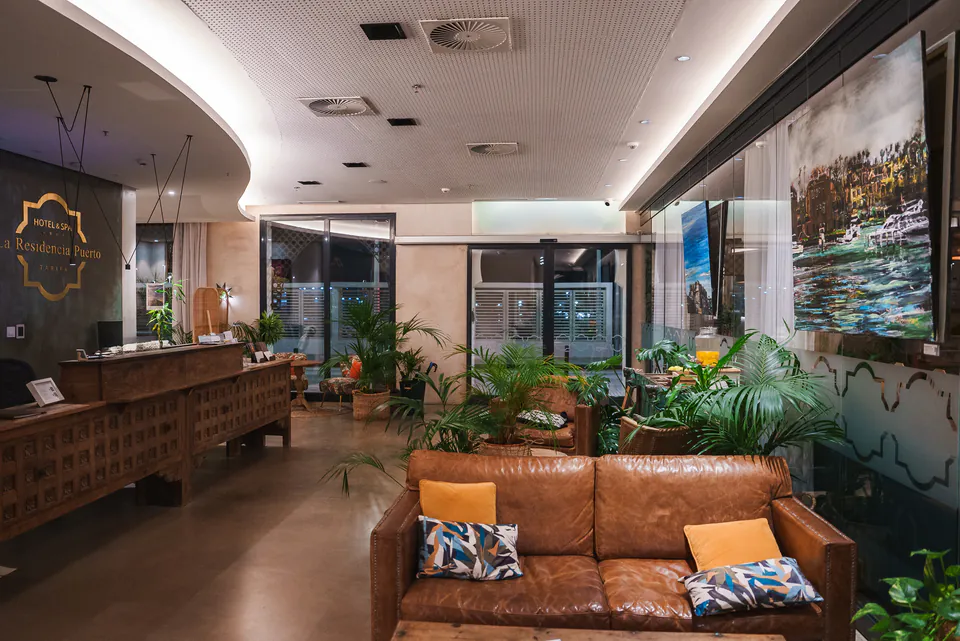 Modern hotel lobby with leather couch, reception desk, and tropical plants