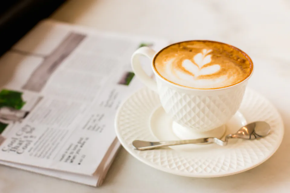 White ceramic coffee cup with latte art on marble table next to menu
