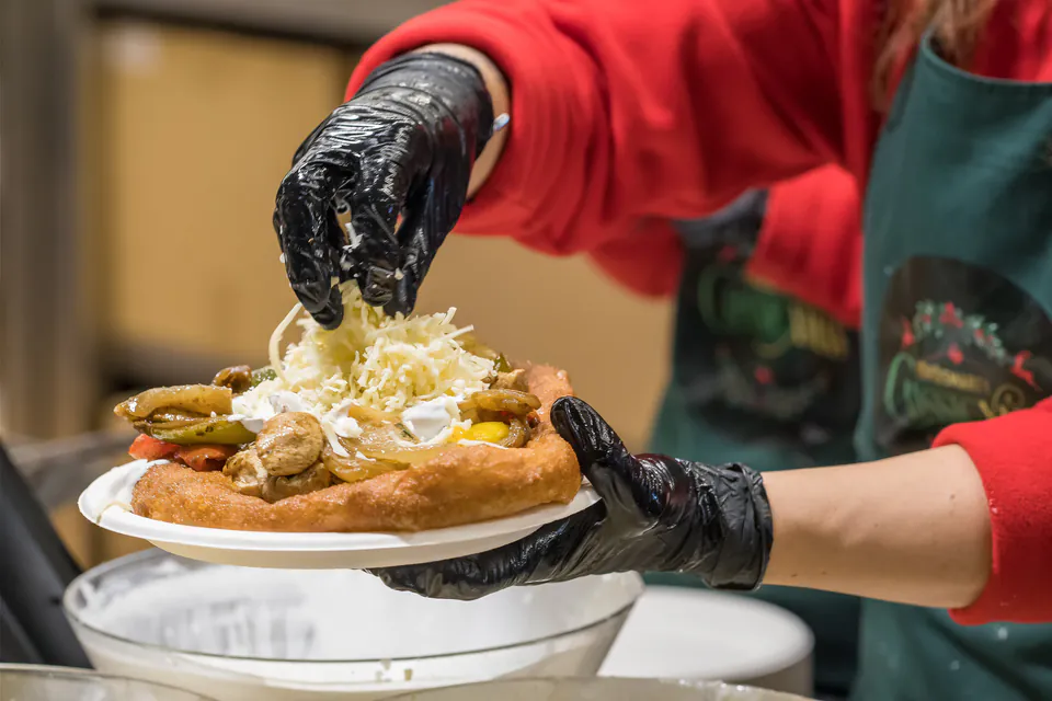 Food vendor preparing traditional Hungarian langos with toppings and cheese