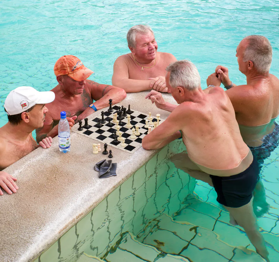 Chess players gathered around floating board in steaming thermal pool waters