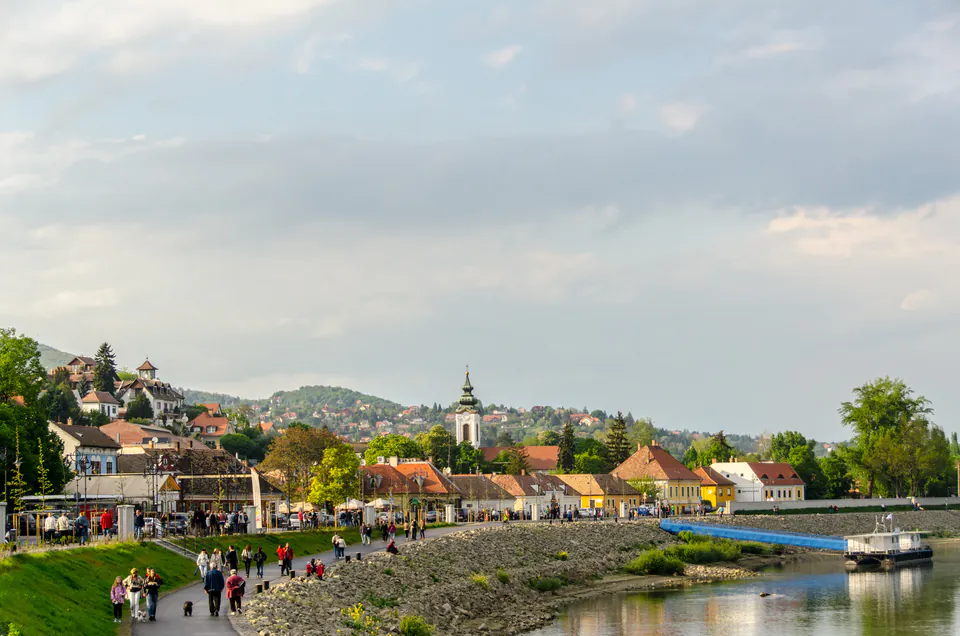 Scenic riverside walkway along Danube River with people strolling and church spires in background