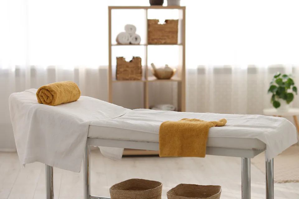 Serene treatment room with massage table, white linens, and wooden storage shelves